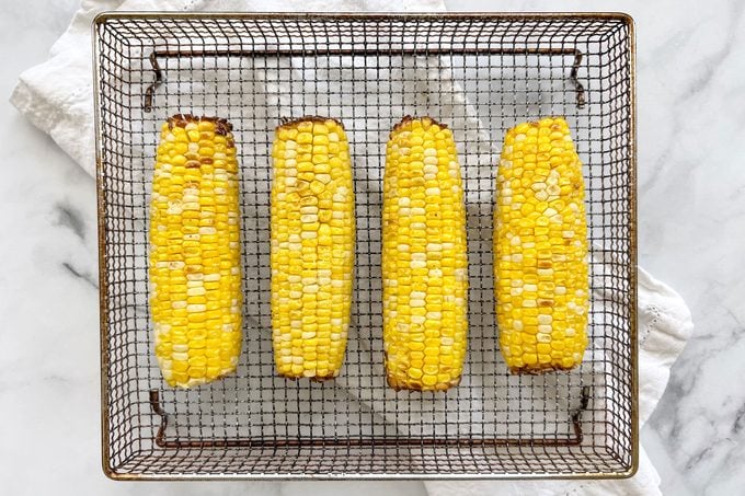 four ears of corn on an air fryer tray after being cooked