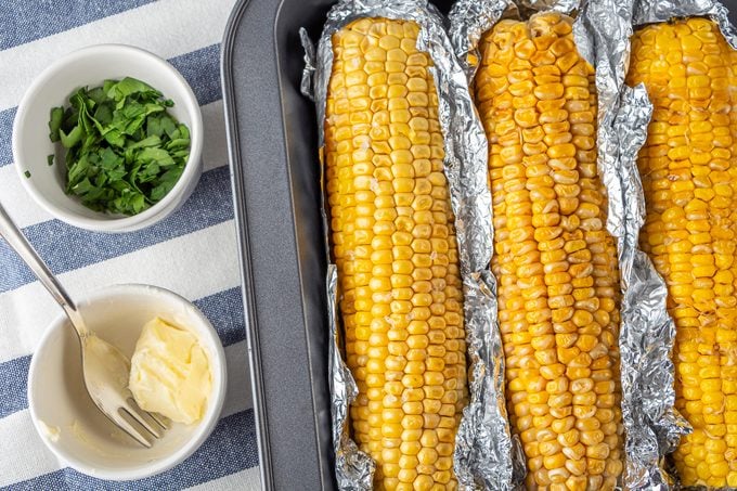 three ears of corn in foil in a pan after being oven roastied