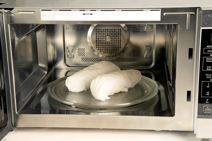 two ears of corn wrapped in paper towels in the microwave